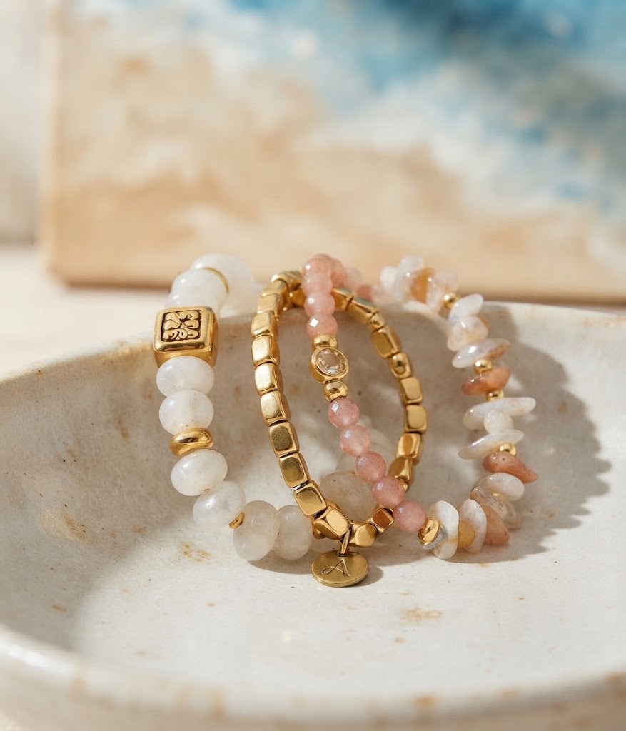 Drie elegante armbanden met parelmoer en roze kralen, goudkleurige accenten op een beige keramisch schaaltje